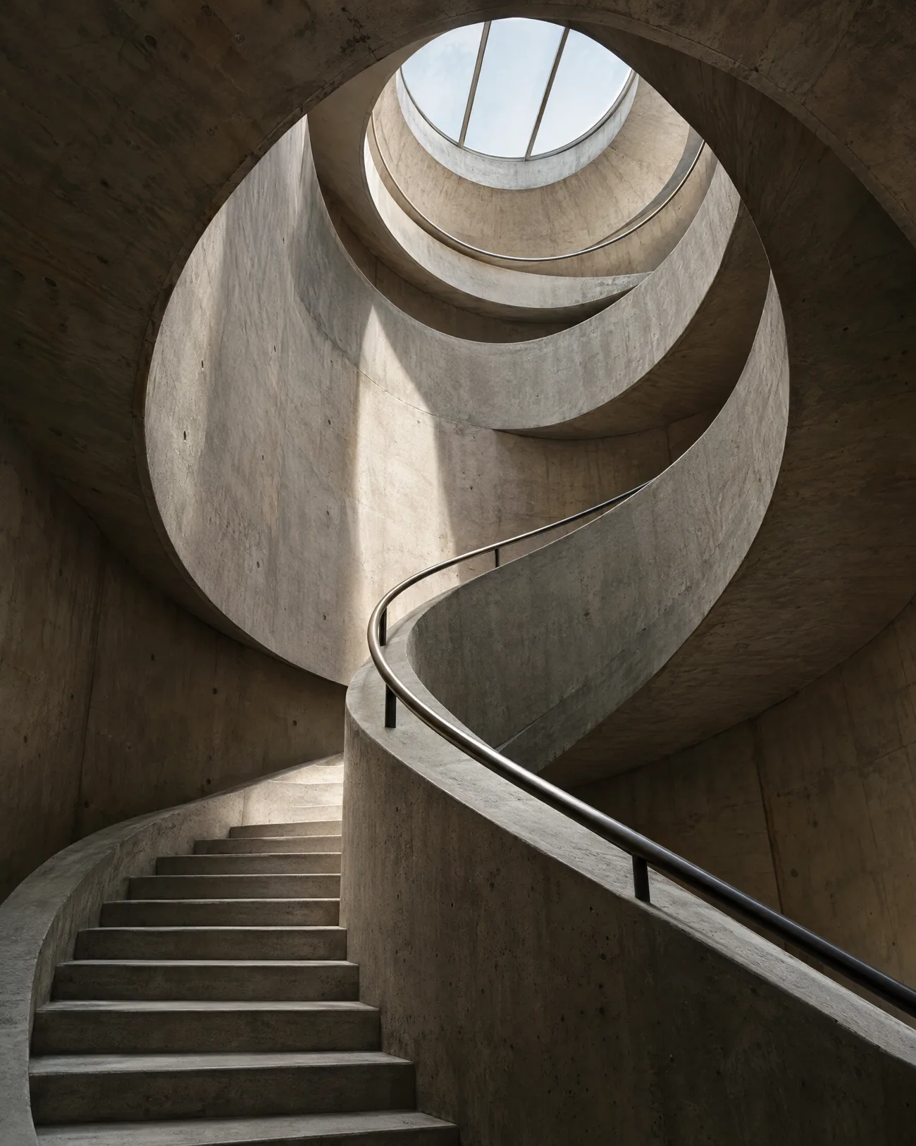 Brutalist concrete spiral staircase lit by a skylight